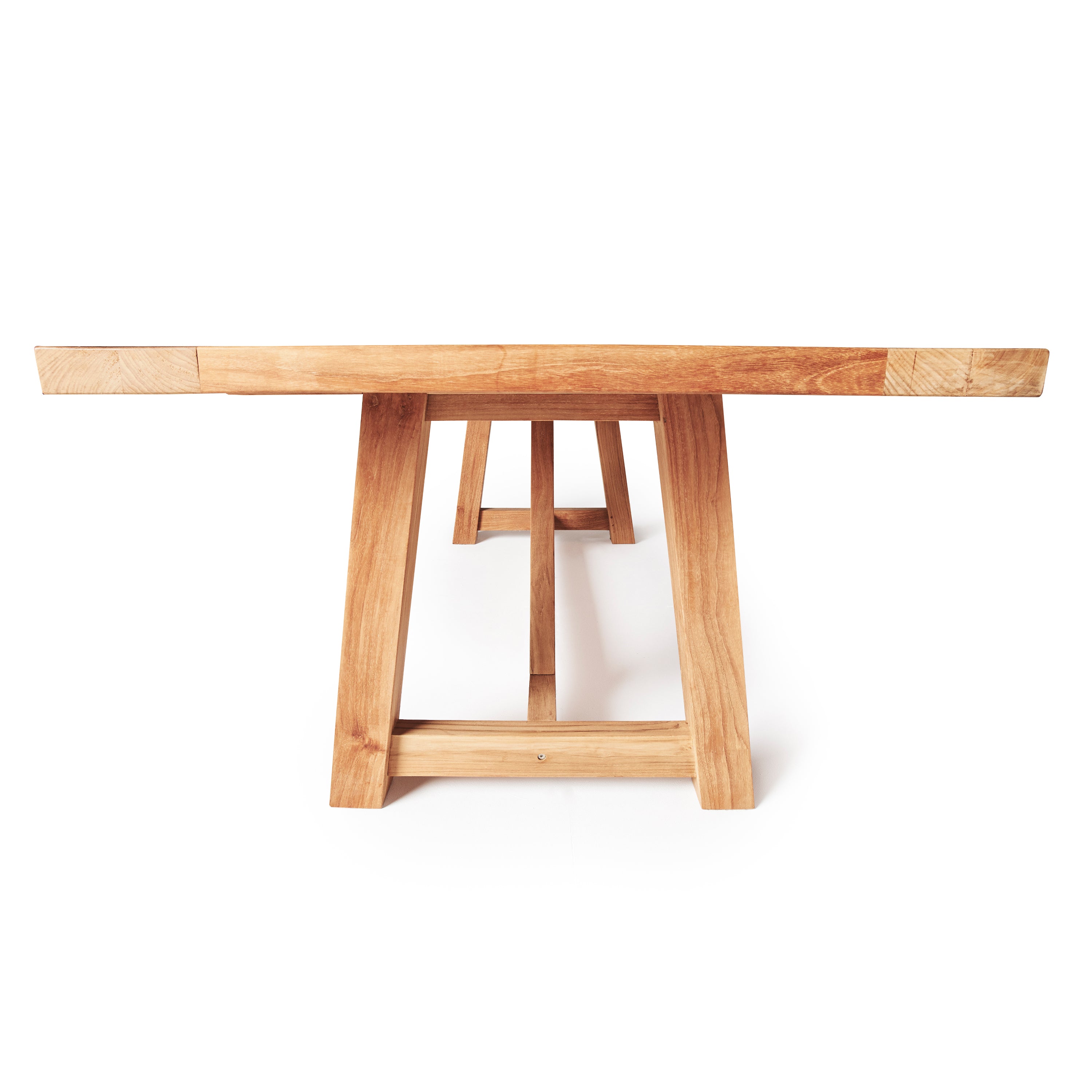 Madera 118" Vintage Beam Table by Terra Outdoor Living is a trestle style dining table with a slatted top. The slats are narrow and elegant. The entire table is made from premium teak in a natural finish. Seats 12. Profile view from height of table.