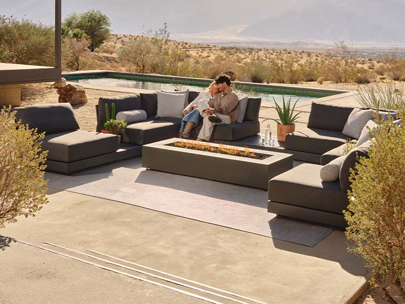 Couple sitting on outdoor furniture by a pool with mountains in the background