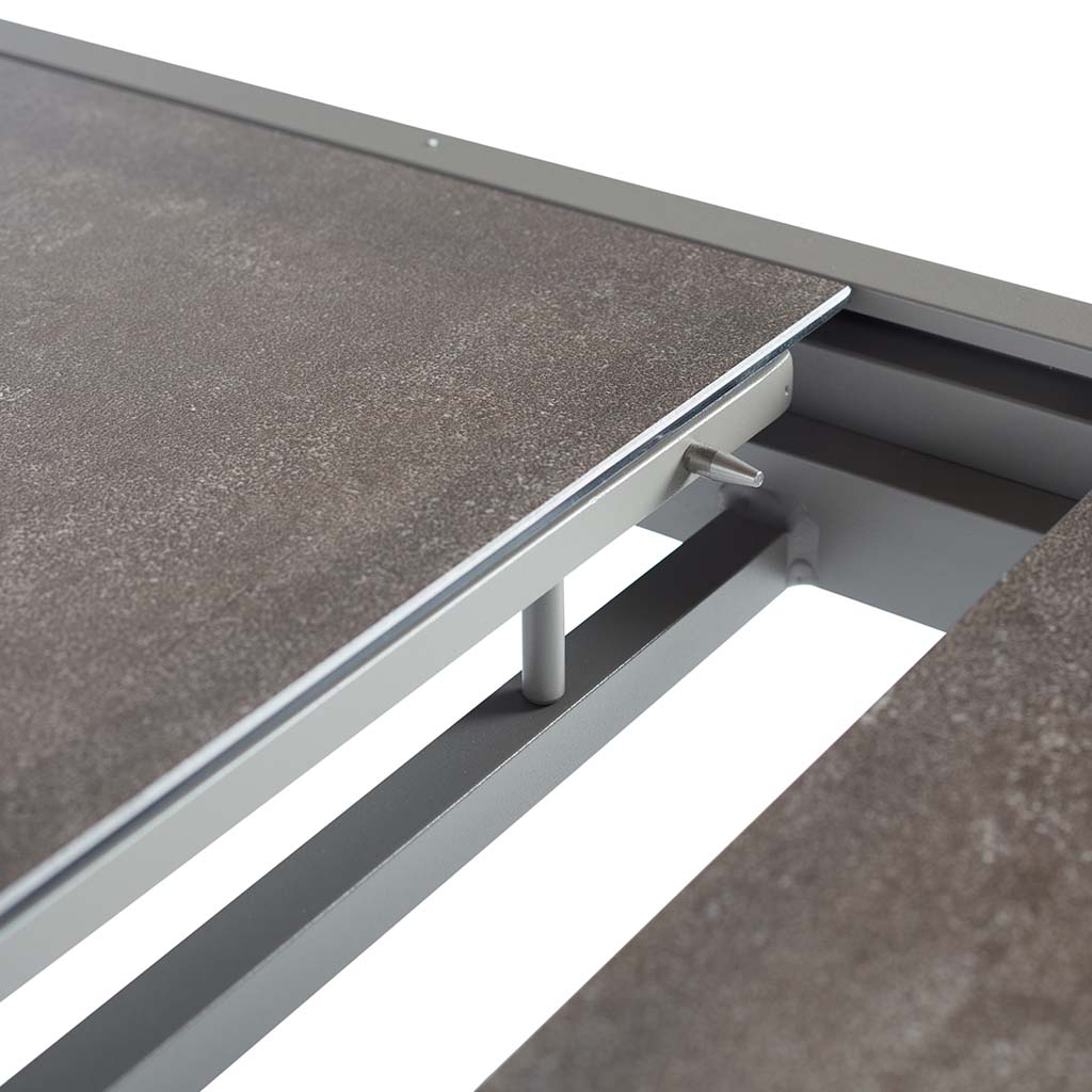 Diablo 87"-130" Extension Dining Table in Quartz Grey by Terra Outdoor Living is an extension dining table, with sled-style powdercoated aluminum frame and 'ceramic' coated tempered safety glass as the table top. It has a sleek modern look and can extend to suit the moment. Image shows table's extension mechanism from above.