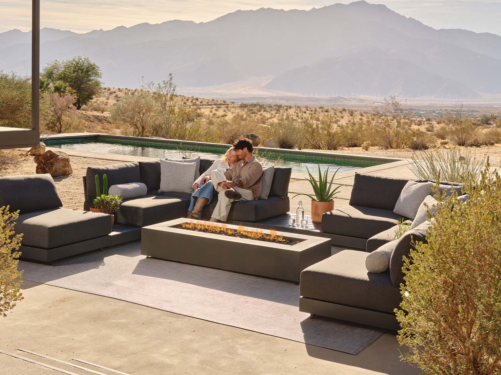 Couple sitting on outdoor furniture by a pool with mountains in the background